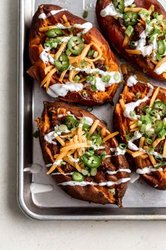 baked sweet potatoes topped with cheese and green onions on a baking sheet, ready to be eaten