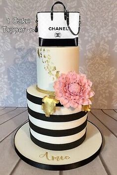 a three tiered cake with black and white stripes, pink flowers and chanel bag on top