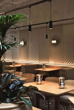 an empty restaurant with wooden tables and plant in the center, along with two large potted plants