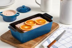 a blue dish with orange slices in it on a cutting board next to other dishes and utensils