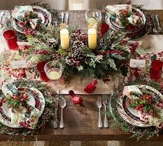 the table is set for christmas dinner with red and white plates, silverware and candles