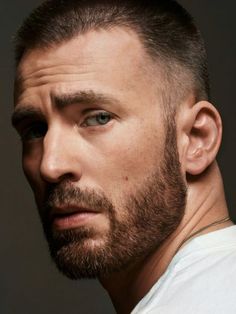 a close up of a man with a beard wearing a white shirt and looking at the camera