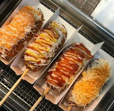 four different types of hot dogs on sticks with cheese and ketchup toppings