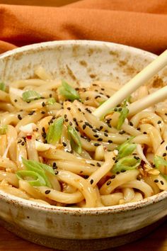 a white bowl filled with noodles and vegetables on top of a wooden table next to chopsticks