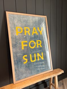 a wooden bench sitting in front of a wall with a sign on it that says pray for sun