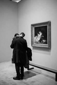 a woman standing in front of a painting on display next to a bench with a coat over her shoulder