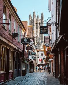 a narrow street with signs and buildings on both sides, in front of a cathedral