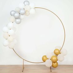 a circle with white and gold balloons in the shape of a wreath on a wooden floor