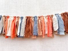 an assortment of different colored scarves hanging from a line on a white wall with linens