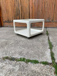 a white table sitting on top of cement ground next to a wooden fence with grass growing under it