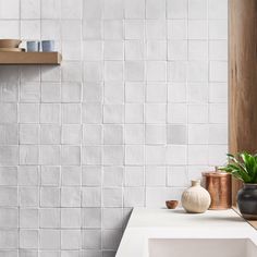 a bathroom with white tiles and wooden shelves on the wall, along with potted plants