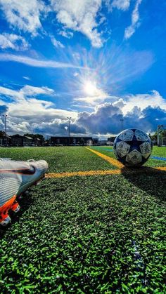 two soccer balls sitting on the ground in front of some grass and blue sky with clouds