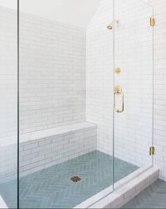 a walk in shower sitting next to a white tiled wall and floor with gold fixtures