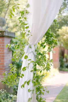 a white curtain with green leaves hanging from it's side in front of a brick building