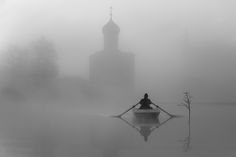 a person in a row boat on a body of water with a church steeple in the background