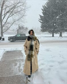 a woman standing in the snow wearing a coat and scarf