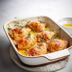 a casserole dish with chicken in it and a small bowl of sauce on the side