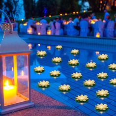 candles are floating on the water in front of a pool with lily pads and lanterns