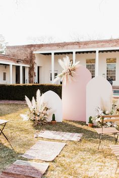 an outdoor setting with chairs, rugs and flowers on the grass in front of a house