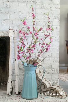 a blue vase filled with pink flowers next to a fireplace