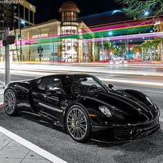 a black sports car is parked on the side of the road at night in front of a building