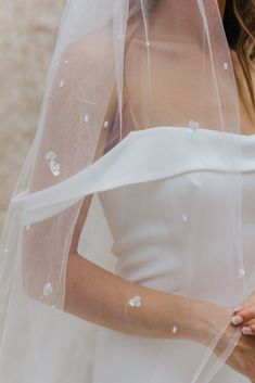 a woman wearing a wedding veil and holding her hand under the veil with white flowers on it