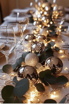 the table is set with silver balls and greenery