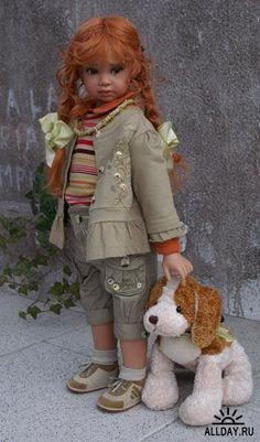 a doll with red hair is holding a stuffed dog in front of a concrete wall