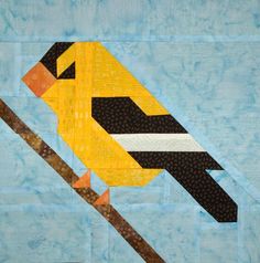 a quilted bird sitting on top of a wooden stick next to a piece of fabric