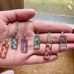 a person is holding four different necklaces in their hand, one with flowers on it