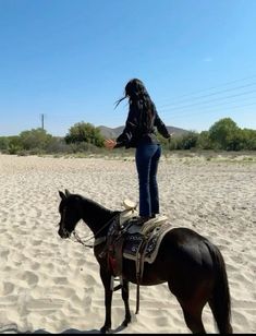 a woman riding on the back of a brown horse across a sandy beach covered in white sand