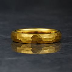 a yellow gold wedding band on a black surface with reflective reflection in the middle,