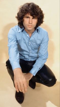 a man sitting on top of a black chair wearing a blue shirt and black pants