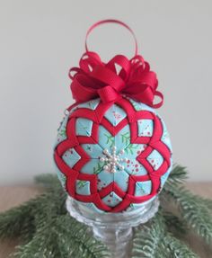 a christmas ornament hanging from a tree branch with red ribbon and bow on it