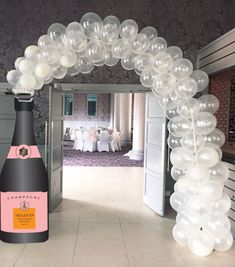 an arch made out of balloons with a bottle of champagne in the middle and tables set up behind it