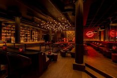 a dimly lit restaurant with red lighting and wooden tables in the foreground, surrounded by bookshelves