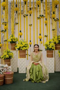 a woman sitting on a chair in front of yellow flowers and hanging garlands with potted plants