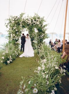 a bride and groom are standing under an arch with white flowers in the foreground