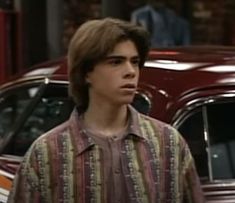 the young man is standing in front of two parked cars and looking off to his left