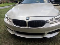 the front end of a white bmw car parked on top of a grass covered field