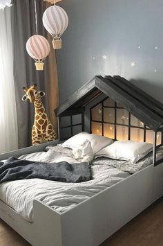 a giraffe standing next to a bed in a room with gray walls and wooden floors