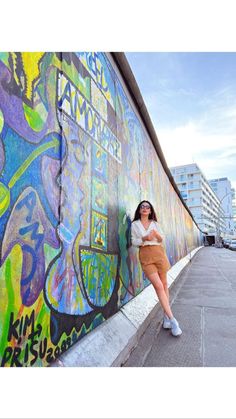 a woman leaning against a wall with graffiti on it's side and her arms behind her back