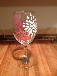 a wine glass with pink and white flowers on it sitting on a wooden table next to a brick wall