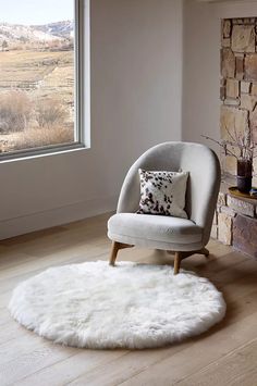 a white chair sitting in front of a window next to a rug on top of a hard wood floor