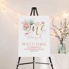 an easel with a welcome sign on it in front of a string of lights