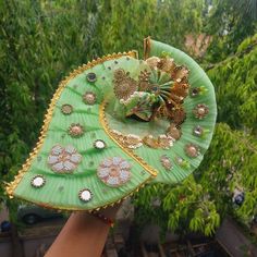 a person holding a green fan with gold decorations on it in front of some trees