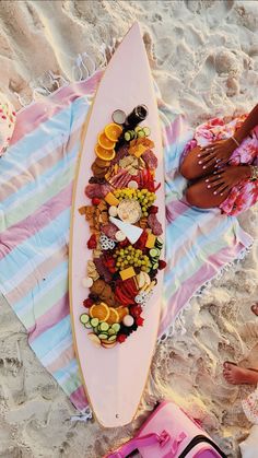 a surfboard covered in lots of different types of candies on the beach next to people