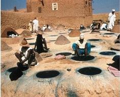 several people sitting on the ground in front of an adobe - style building with round holes