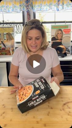 a woman holding a box of pizza on top of a wooden table