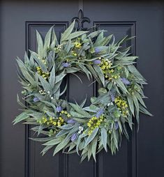 a wreath on the front door of a house with green leaves and yellow flowers hanging from it